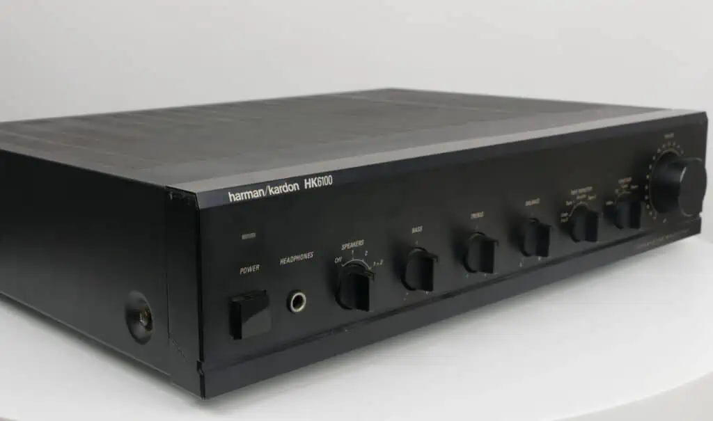 Harman/Kardon HK6100 stereo versterker in zwart met zichtbare gebruikssporen op een witte achtergrond.